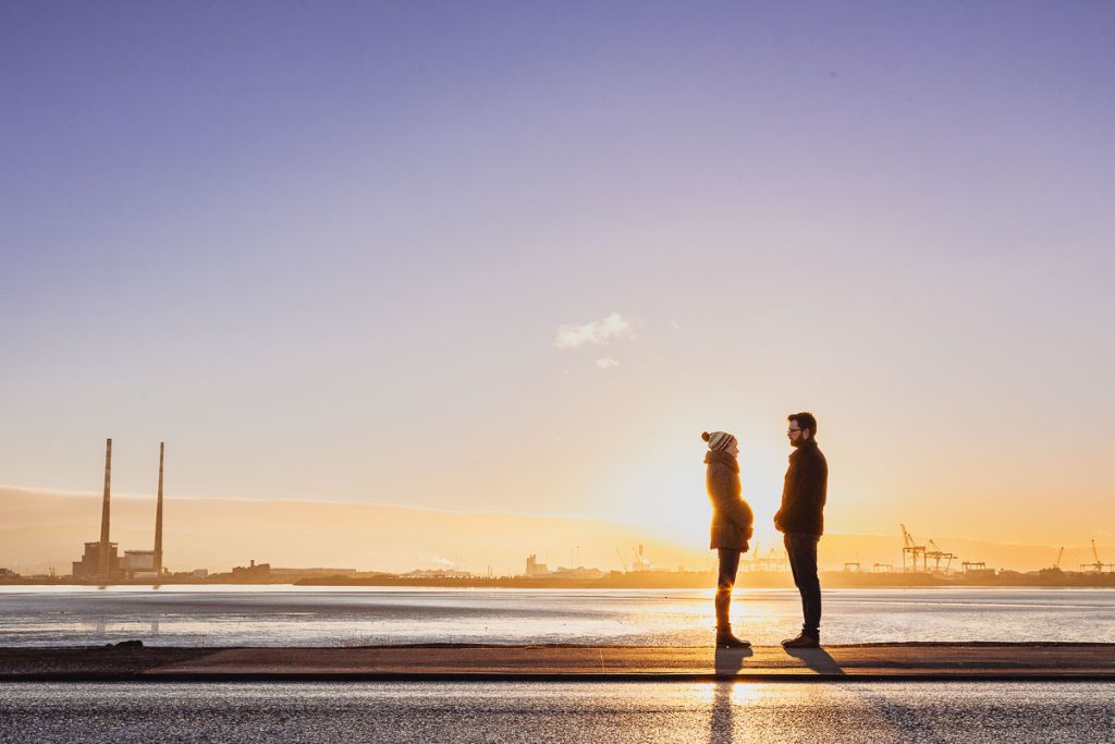 Silouette of a Young couple expecting baby, stand looking at each other with sunset behind them.